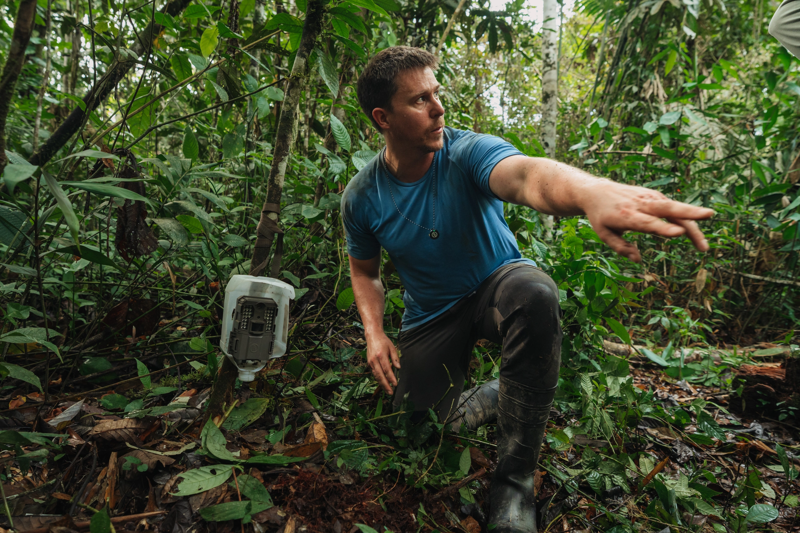 Field researcher beside a camera trap on the forest floor in Manu